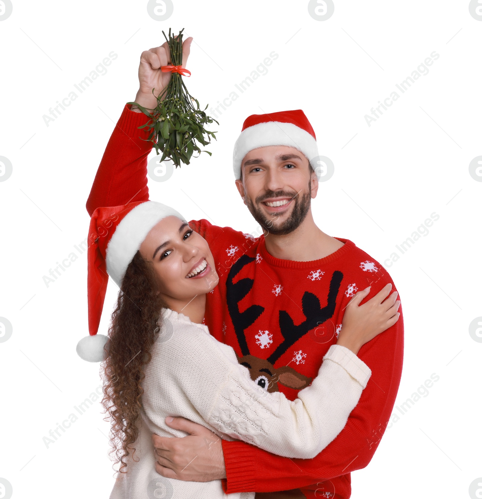 Photo of Portrait of lovely couple in Santa hats under mistletoe bunch on white background