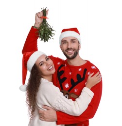 Photo of Portrait of lovely couple in Santa hats under mistletoe bunch on white background