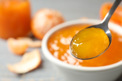 Photo of Teaspoon with tasty tangerine jam over table, closeup. Space for text