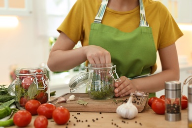 Photo of Woman putting dill into pickling jar at table in kitchen, closeup