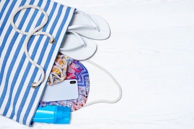 Flat lay composition with beach bag and accessories on white wooden background, space for text
