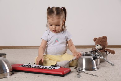 Photo of Cute little girl with cookware and toy piano at home