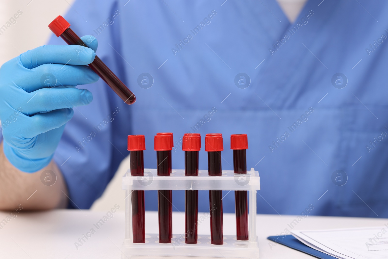 Photo of Doctor with samples of blood in test tubes at white table, closeup