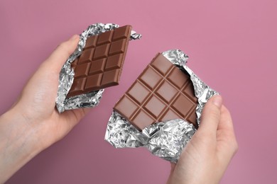 Woman holding parts of delicious chocolate bar on pink background, closeup