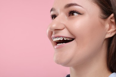 Smiling woman with dental braces on pink background, closeup. Space for text