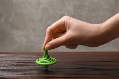 Photo of Woman playing with green spinning top at wooden table, closeup