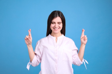 Photo of Happy young woman crossing fingers on light blue background. Dealing with stress