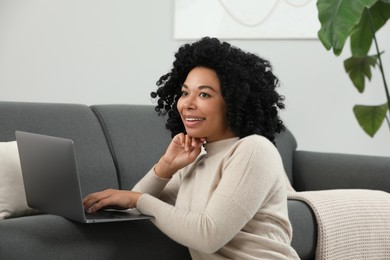 Happy young woman using laptop on sofa indoors