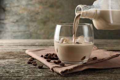 Photo of Pouring coffee cream liqueur into glass at wooden table, closeup