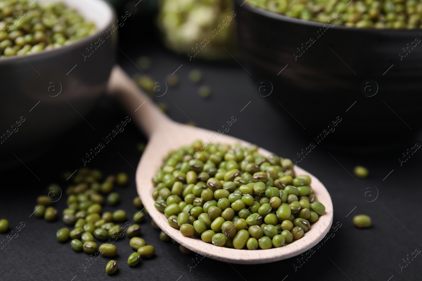 Photo of Different dishware with green mung beans on black background, closeup