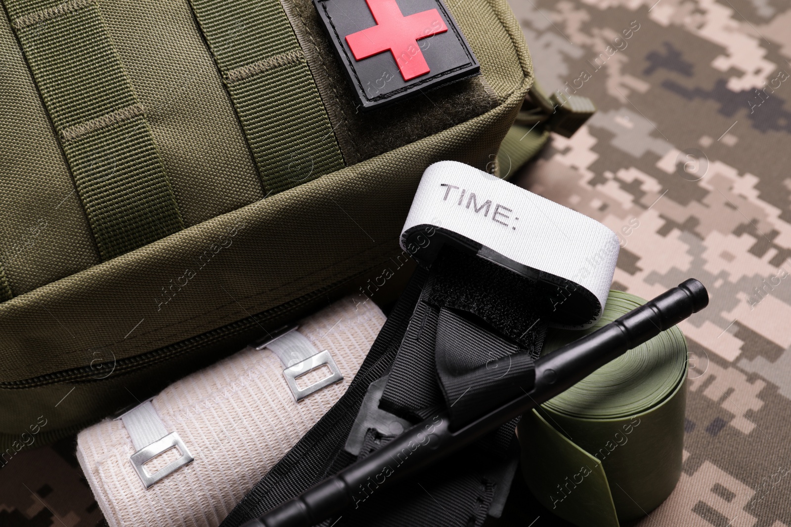 Photo of First aid kit with medical tourniquet and elastic bands on military fabric, closeup