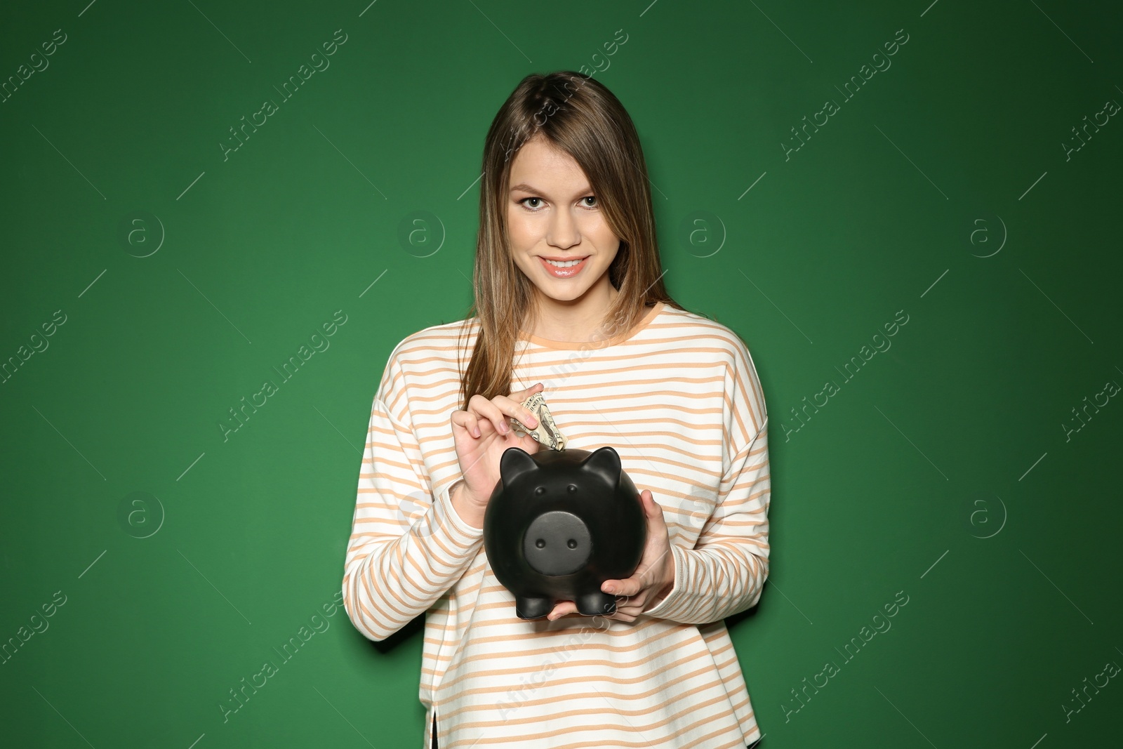 Photo of Young woman putting money into piggy bank on color background