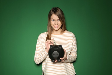 Photo of Young woman putting money into piggy bank on color background
