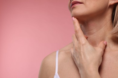 Photo of Woman touching her neck on pink background, closeup. Space for text