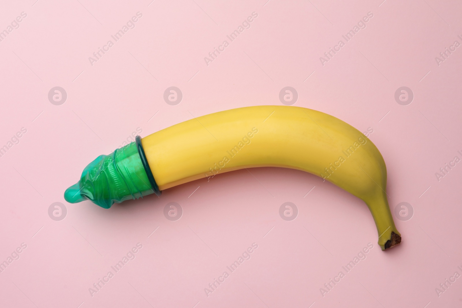 Photo of Banana with condom on pink background, top view. Safe sex concept