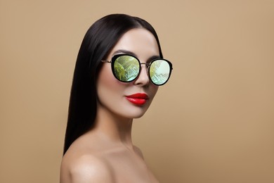 Image of Attractive woman in stylish sunglasses on dark beige background. Palm leaves and sky reflecting in lenses. Space for text