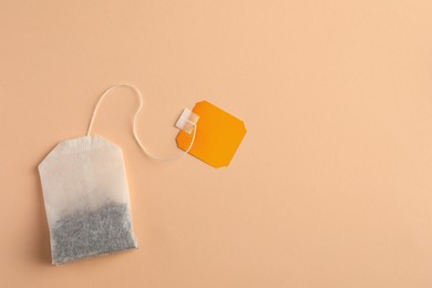 New tea bag with tab on pale orange background, top view. Space for text