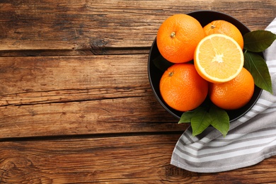 Delicious ripe oranges in bowl on wooden table, top view. Space for text