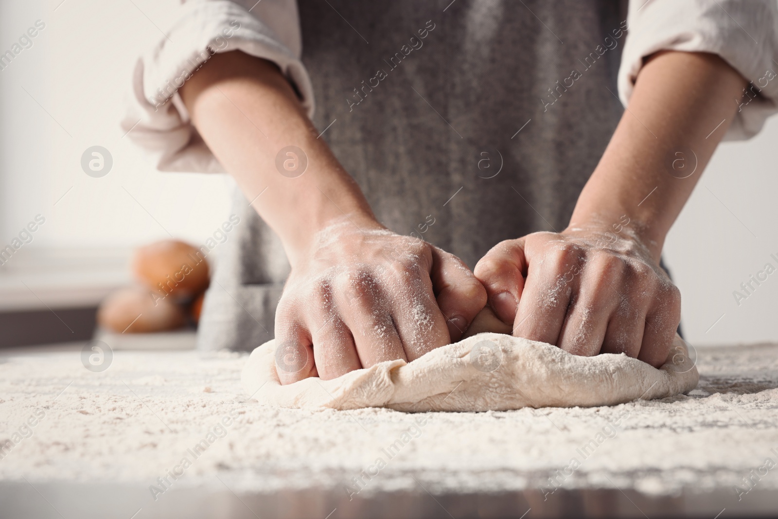 Photo of Woman kneading dough at table in kitchen, closeup