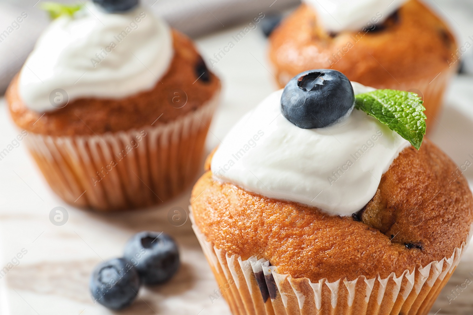 Photo of Tasty muffins, cream and blueberries on table, closeup