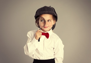 Cute little child in hat with magnifying glass playing detective on color background