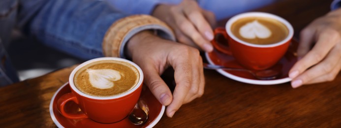 Image of Couple with cups of aromatic coffee at wooden table, closeup. Banner design