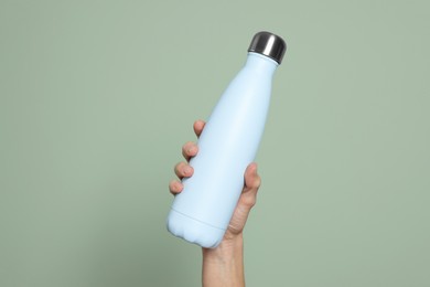 Woman holding thermo bottle on green background, closeup