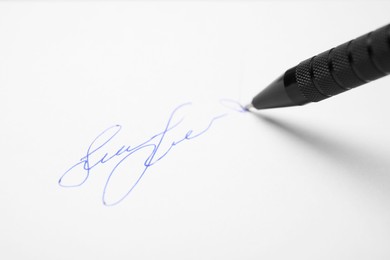 Signing on sheet of white paper with pen, closeup