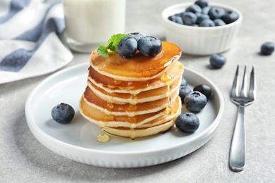 Photo of Plate of tasty pancakes with blueberries and honey on light grey table