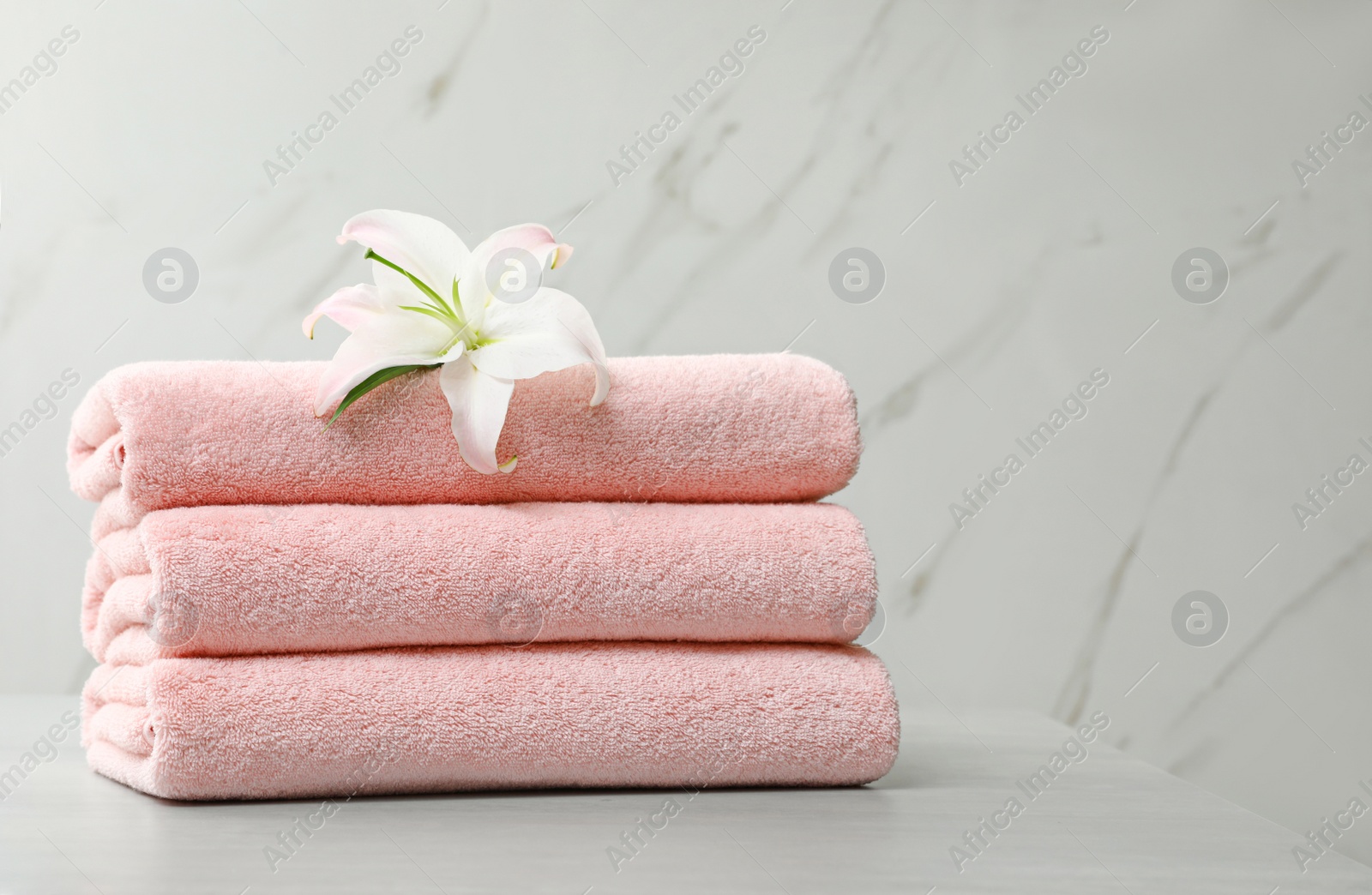 Photo of Stack of fresh towels with flower on grey table against light background. Space for text