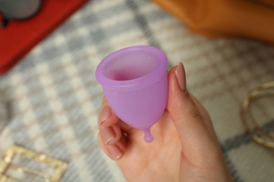 Woman holding violet menstrual cup on blurred background, closeup