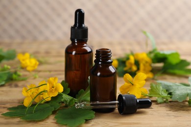 Bottles of natural celandine oil near flowers on wooden table