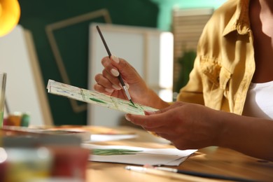 Photo of Young woman drawing leaf at table indoors, closeup