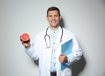 Photo of Nutritionist with ripe grapefruit and clipboard on light grey background
