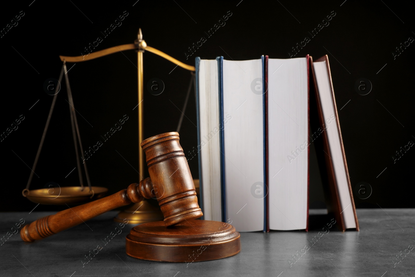 Photo of Judge's gavel, books and scales on grey table against black background. Criminal law concept