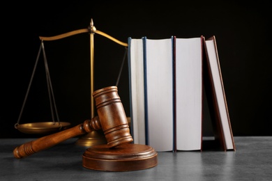 Judge's gavel, books and scales on grey table against black background. Criminal law concept