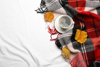 Flat lay composition with hot drink and warm plaid on white bedsheet, space for text