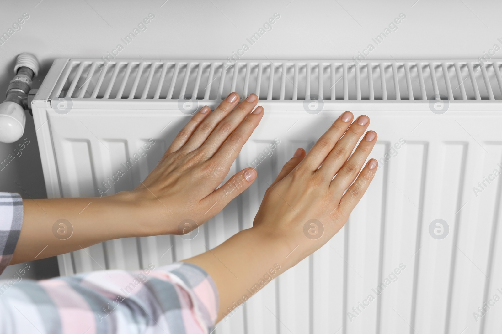 Photo of Woman warming hands on heating radiator near white wall, closeup