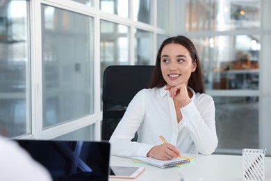 Happy woman taking notes at white desk in open plan office, space for text