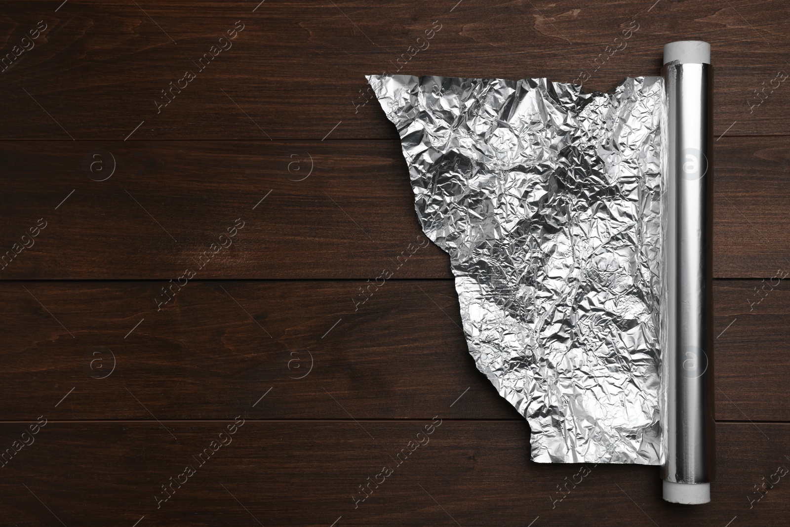 Photo of Roll of foil paper on wooden table, top view. Space for text