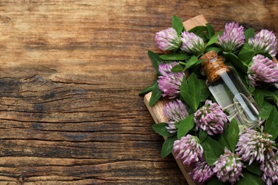 Photo of Beautiful clover flowers and bottle of essential oil on wooden table, above view. Space for text