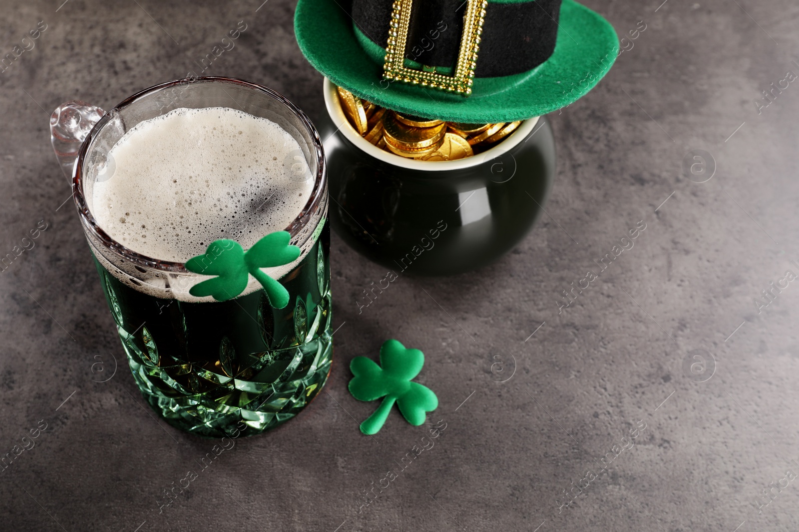 Photo of St. Patrick's day celebration. Green beer, leprechaun hat, pot of gold and decorative clover leaves on grey table. Space for text