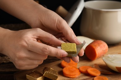Photo of Woman holding bouillon cube at table, closeup