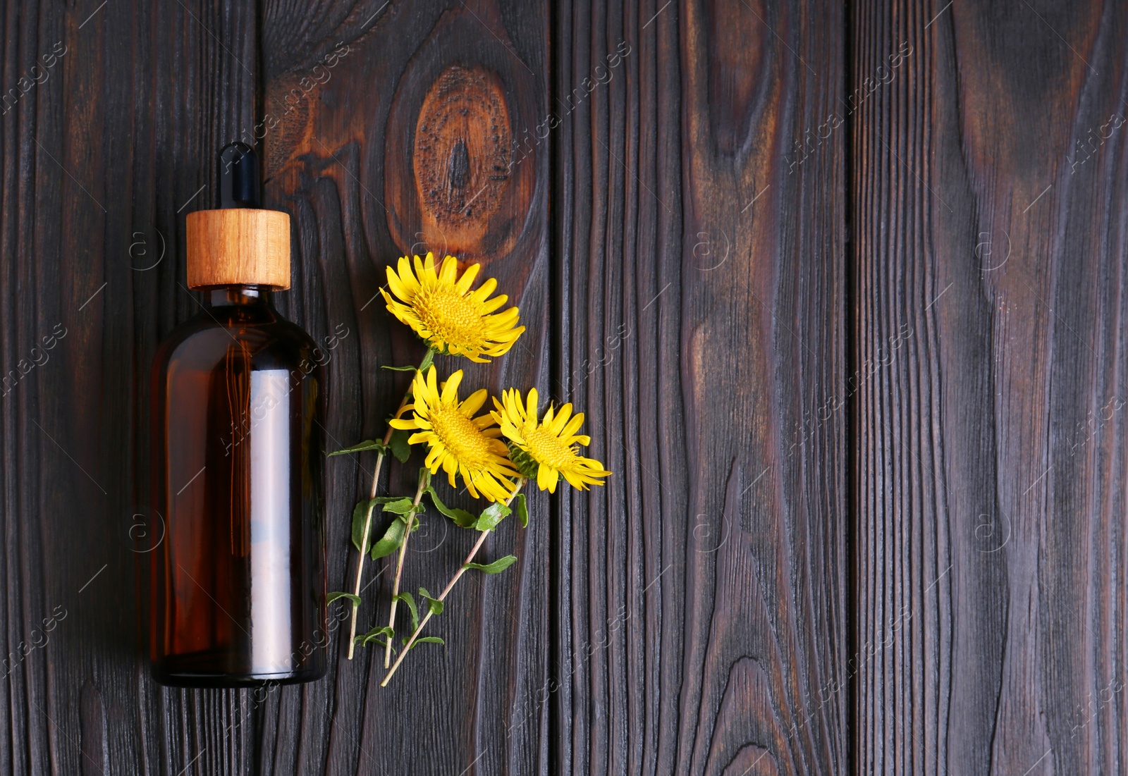 Photo of Glass bottle of aromatic essential oil and yellow wildflowers on wooden table, flat lay. Space for text