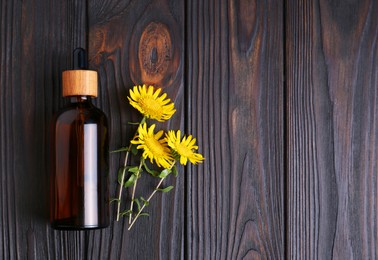 Photo of Glass bottle of aromatic essential oil and yellow wildflowers on wooden table, flat lay. Space for text