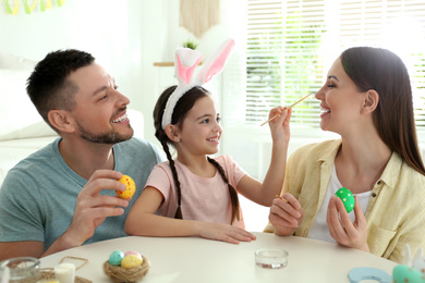 Happy father, mother and daughter having fun while painting Easter eggs at table indoors