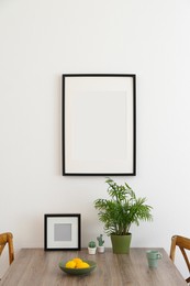 Photo of Room interior with dining table, wooden chairs and photo frames on white wall