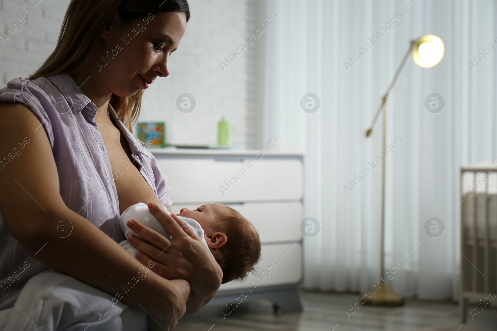 Photo of Young woman breast feeding her little baby at home. Space for text