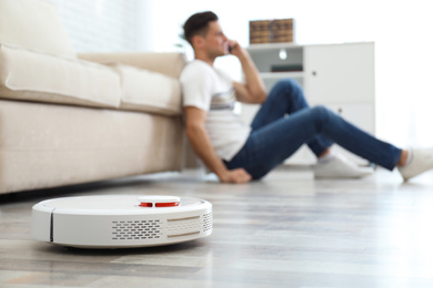 Photo of Man talking on phone while robotic vacuum cleaner doing his work at home