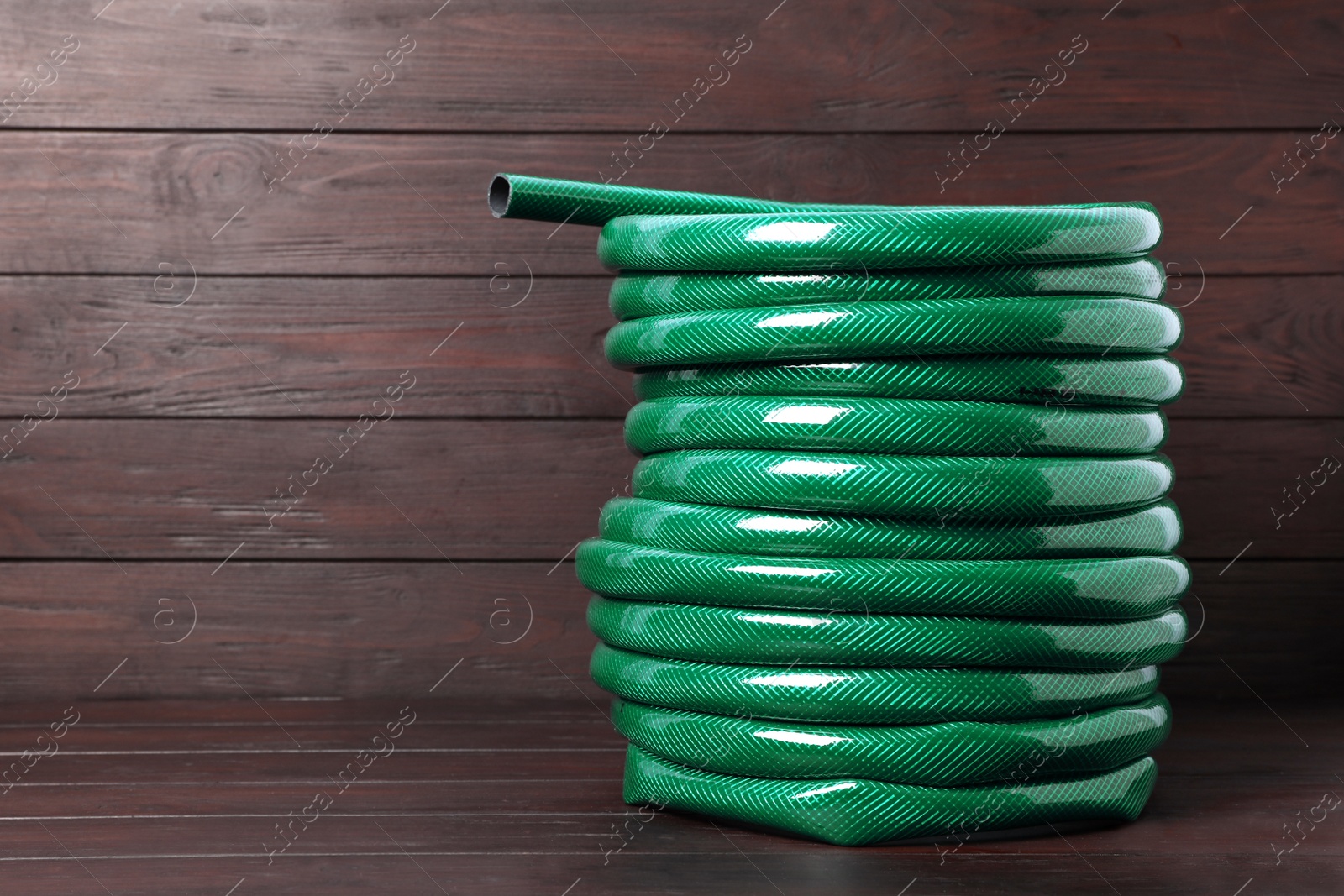 Photo of Green garden hose on wooden table, space for text